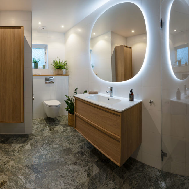 Renoverat badrum med dusch - skåp, toalett och kommod med lysande spegel över
